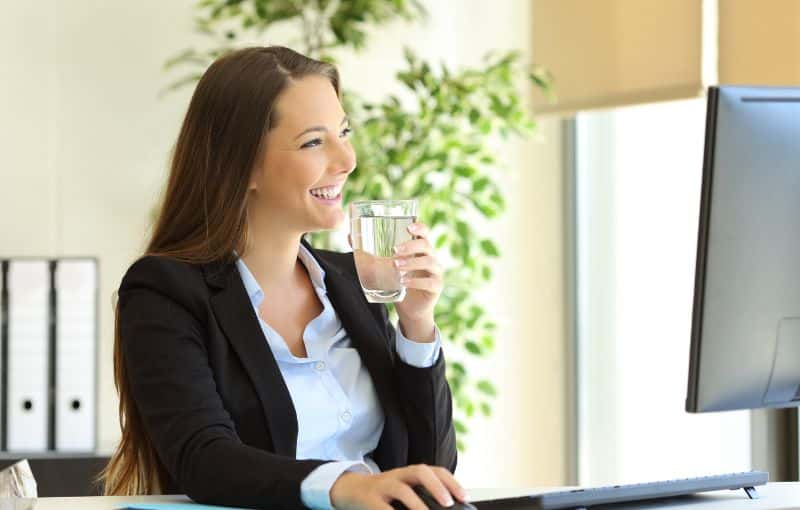 Femme qui boit de l'eau derrière son bureau